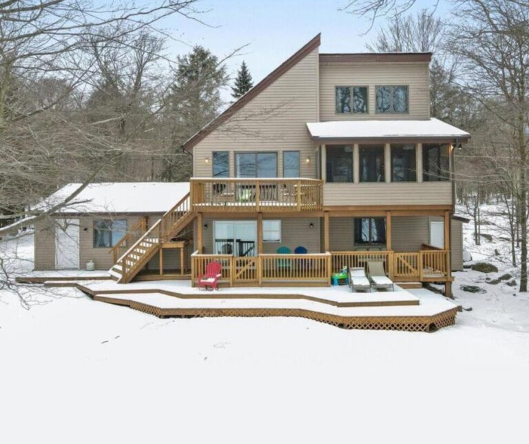 Modern home with a multi-level deck overlooking a snowy yard, set among trees; ideal for winter retreats or cozy gatherings.
